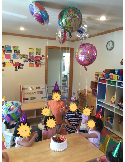 Children gathered around a birthday cake in the daycare playroom; their faces have stickers