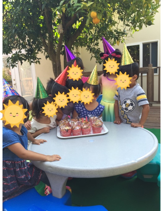 A birthday celebration at a table in the shaded backyard; children’s faces have stickers