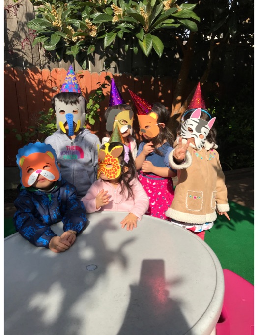 Children in colorful costumes gathered at an outdoor table; their faces have stickers