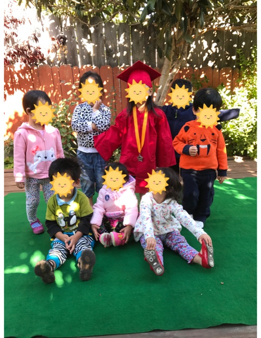 A caregiver and children standing under the backyard trees; the children’s faces have stickers