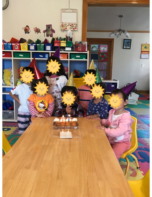 Children gathered at the daycare table for a birthday; their faces have stickers