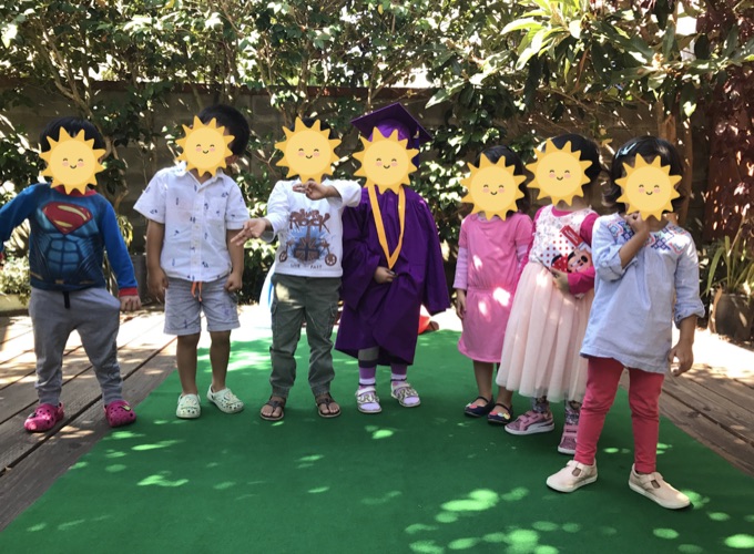 Children standing together under the backyard fruit trees; their faces have stickers
