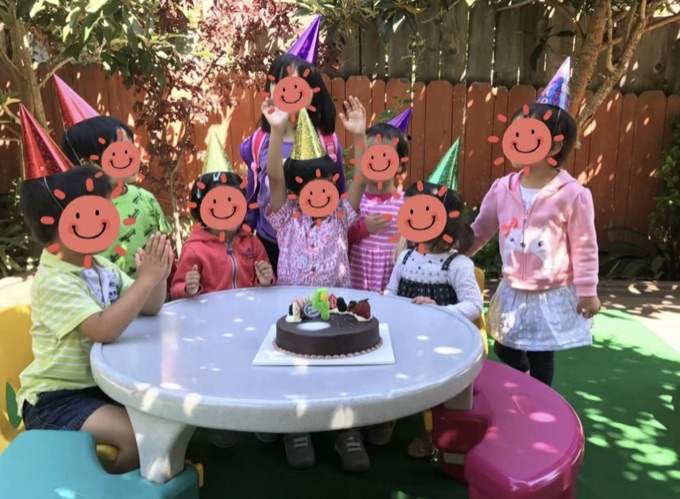 Children wearing party hats at a backyard birthday table; their faces have stickers