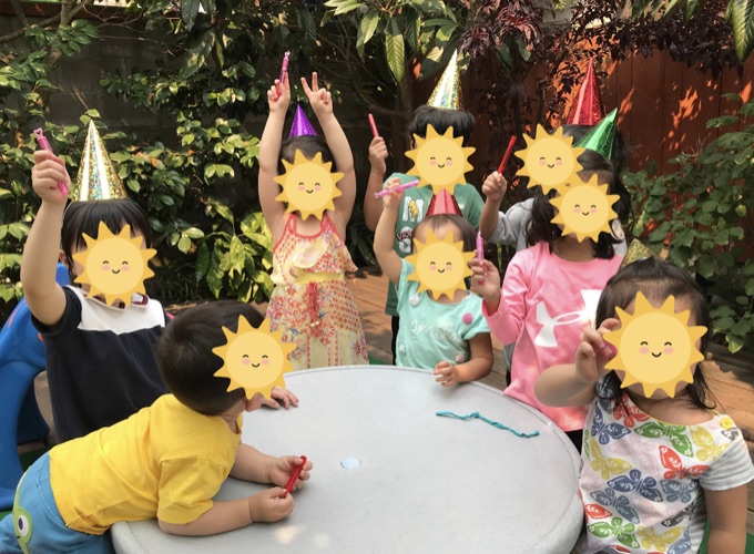 Children celebrating together around an outdoor table; their faces have stickers